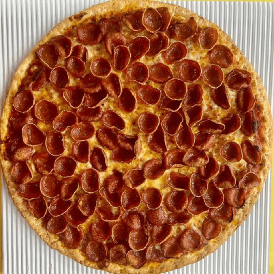 A whole, round Casa Di Pizza pepperoni pizza with a golden crust on a striped surface.